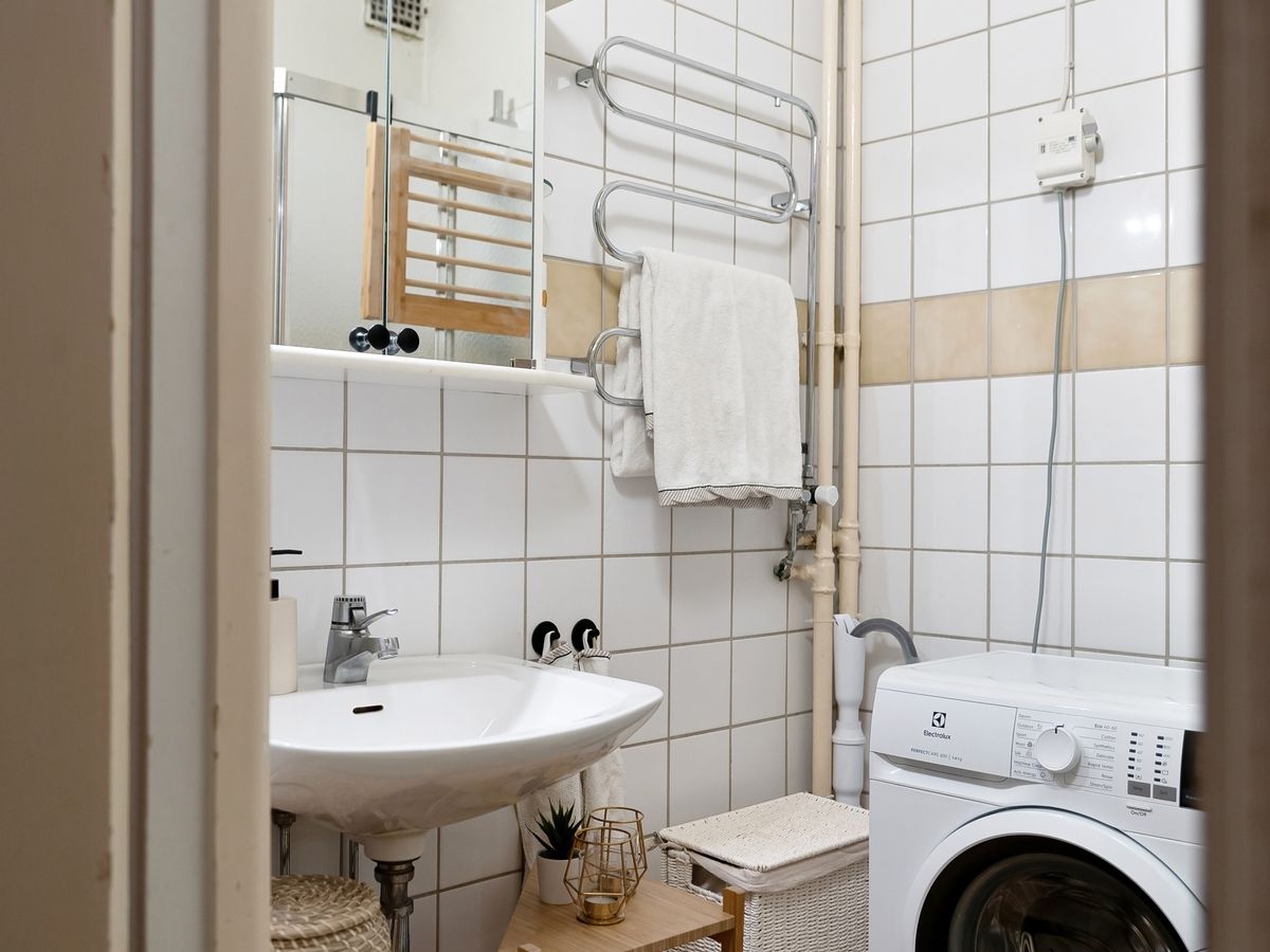 Compact bathroom with washing machine and wooden shelving used to organize laundry supplies
