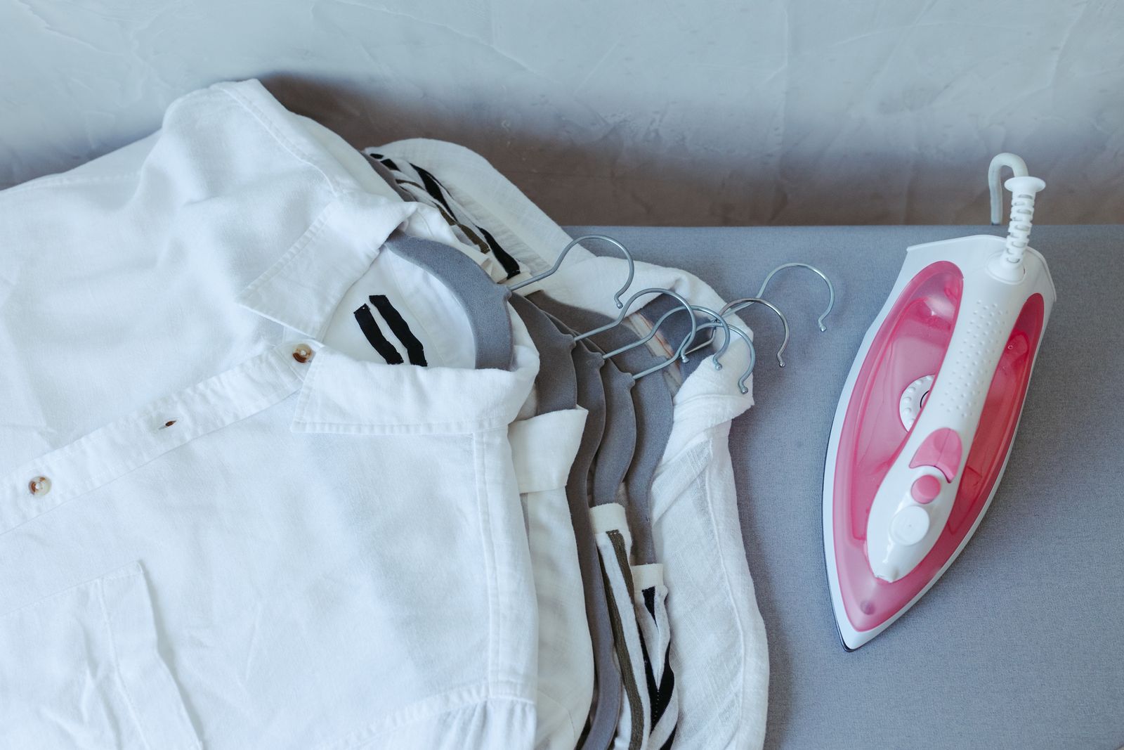Folded white dress shirts next to an iron ready for pressing