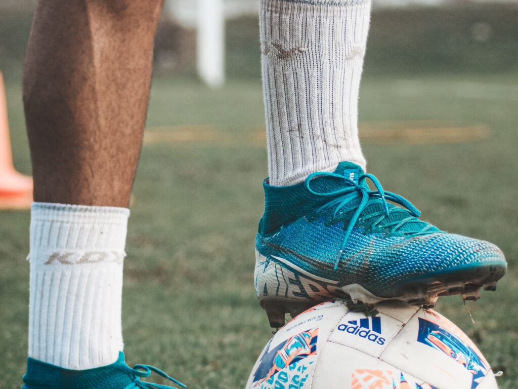 Soccer cleats and ball on a grassy field where grass and mud stains happen