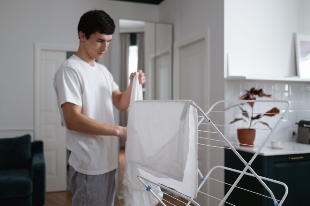 Man hanging washed clothes on an indoor drying rack