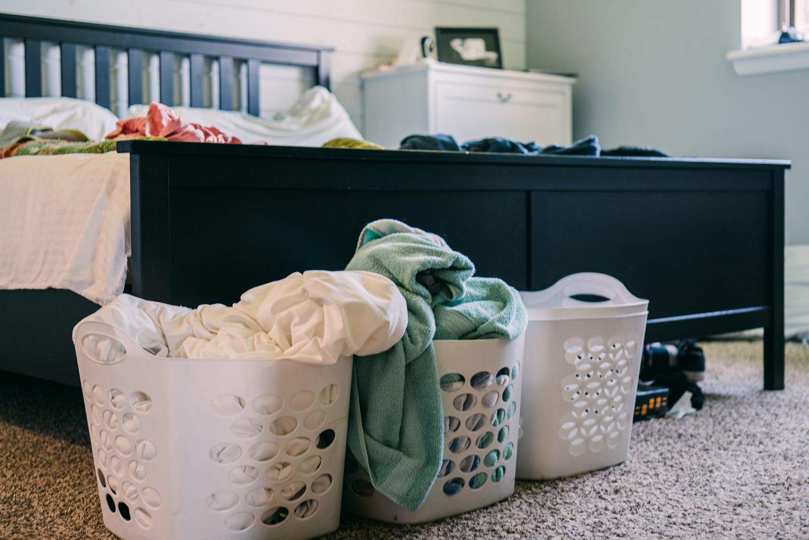 Laundry baskets with bedding beside a bed before washing bed sheets