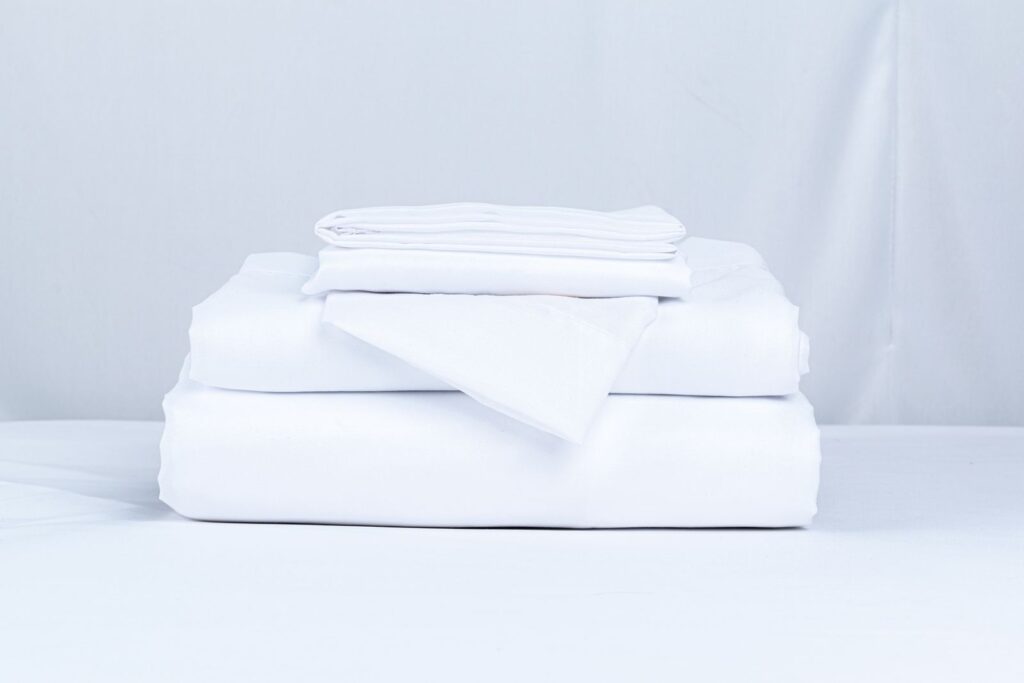 Neatly folded stack of clean white bed sheets ready to wash
